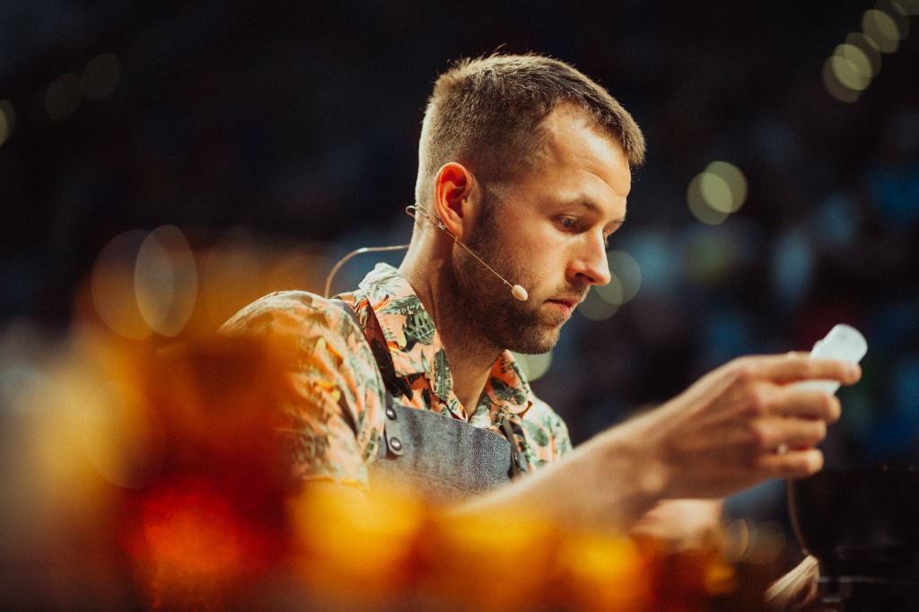 Barista v zástěře s headsetem se soustředí při soutěžním výkonu.